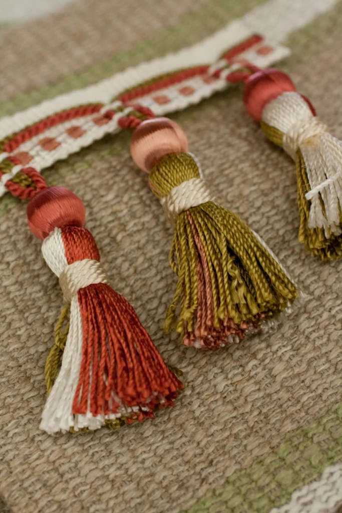 Coral, olive and cream decorative tassels arranged on a woven neutral textile