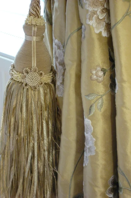 A large cream curtain tassel hanging against embroidered golden fabric