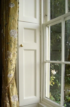 Tall white-paned window framed by golden embroidered curtains and a garden view