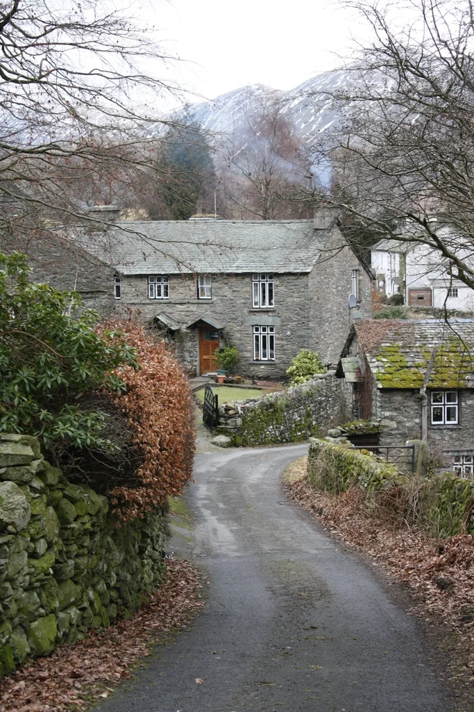 A slate-roofed stone cottage at the end of a lane beneath a wooded mountain