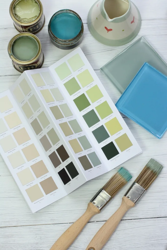 An open paint colour book beside sample pots and two decorators' brushes