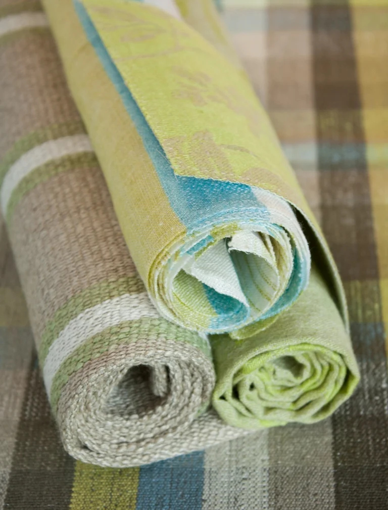 Three rolled fabric samples in lime, blue and natural green tones