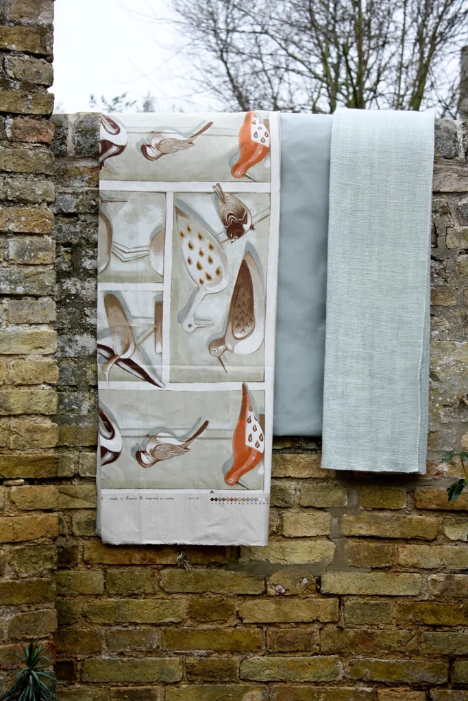 Bird-print fabric and a pale blue textile draped over an old stone garden wall