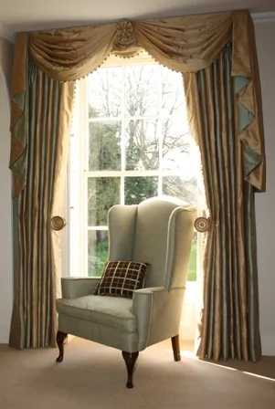 An upholstered armchair positioned in front of a dressed window with a tailored pelmet